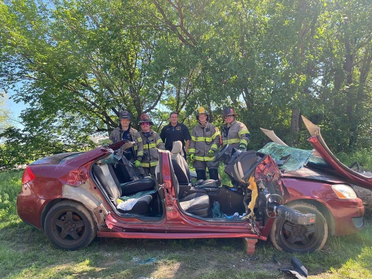 A group of firefighters are standing next to a wrecked car.
