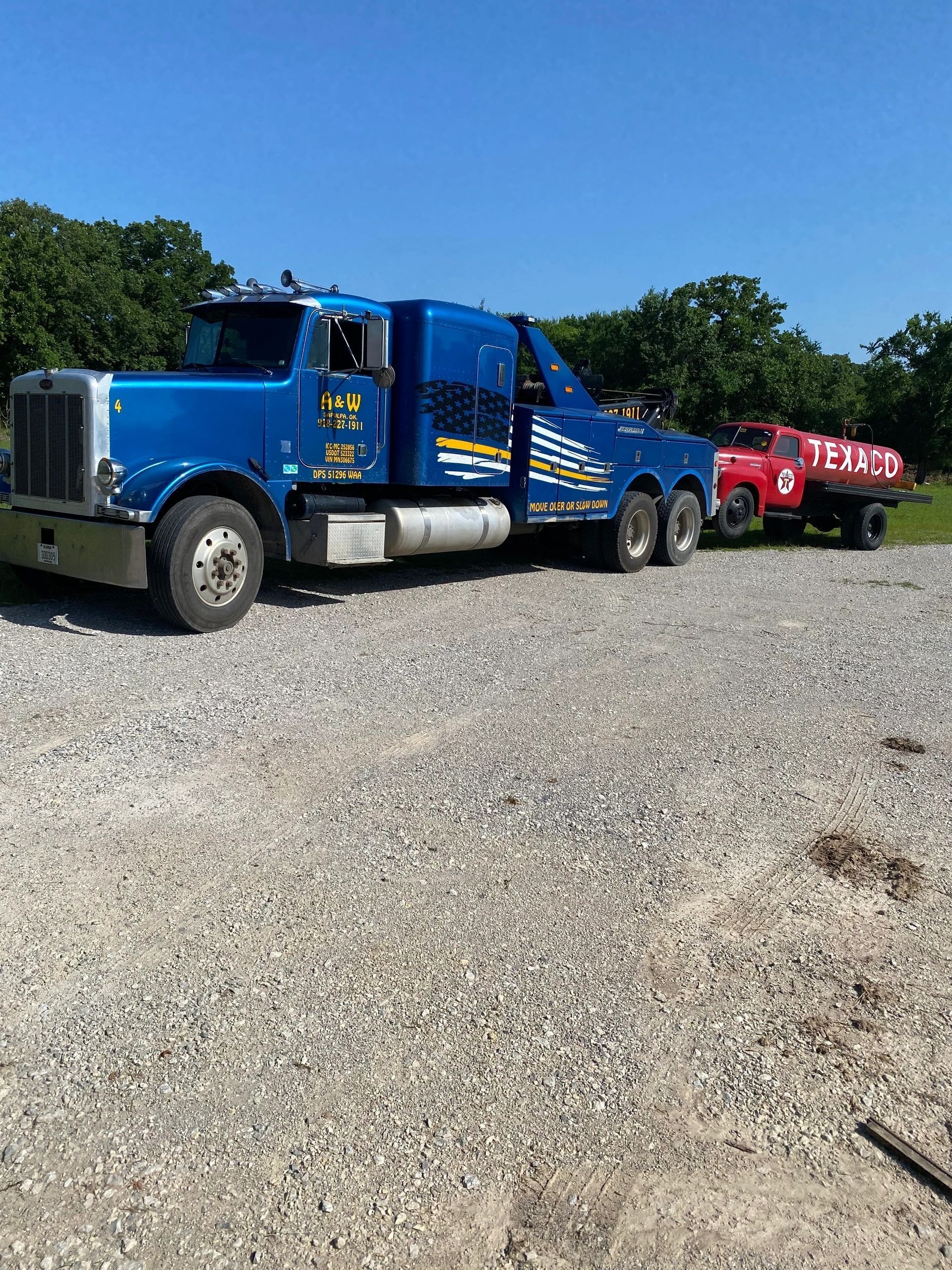 A blue tow truck is parked next to a red truck in a gravel lot.