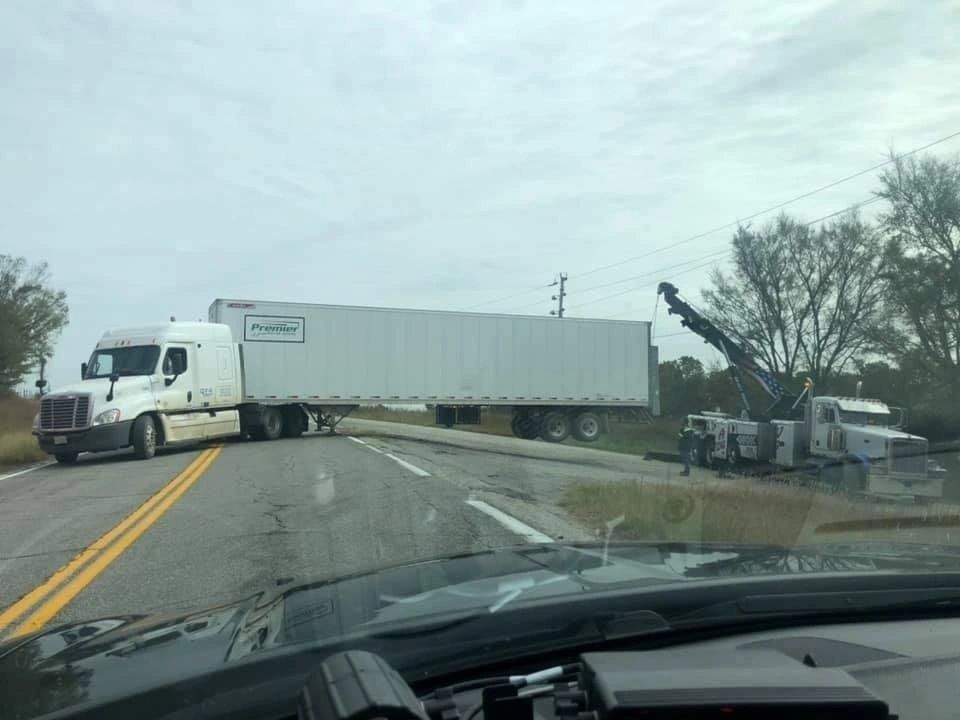 A white semi truck is driving down a highway next to a tow truck.