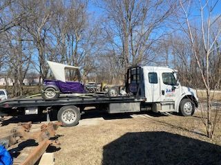 A tow truck is carrying a purple buggy on the back of it.