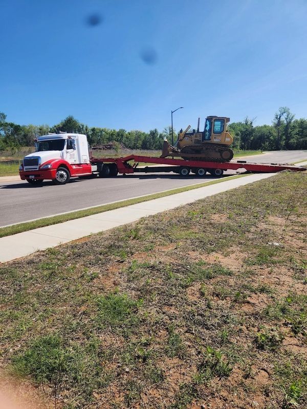 A red and white semi truck is carrying a bulldozer on a trailer.