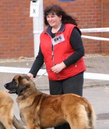 Woman in red vest standing with a German shepherd outdoors near a brick wall