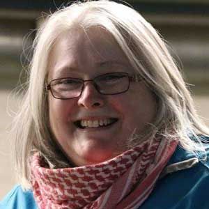 Smiling person with glasses and a red patterned scarf, wearing a blue jacket outdoors