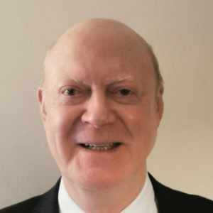 Smiling bald man in a suit and tie against a plain beige background