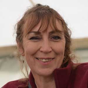 Smiling woman in a burgundy jacket outdoors with a blurred background