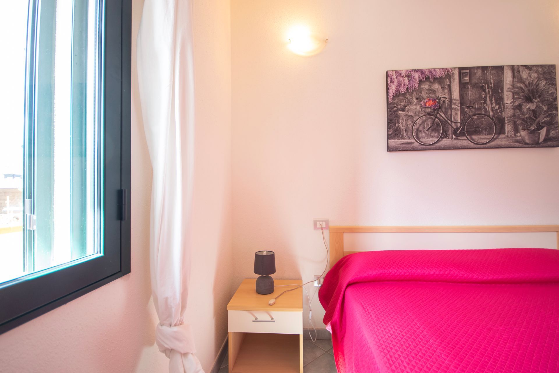 Una camera da letto con un letto, un comodino, una lampada e una finestra.