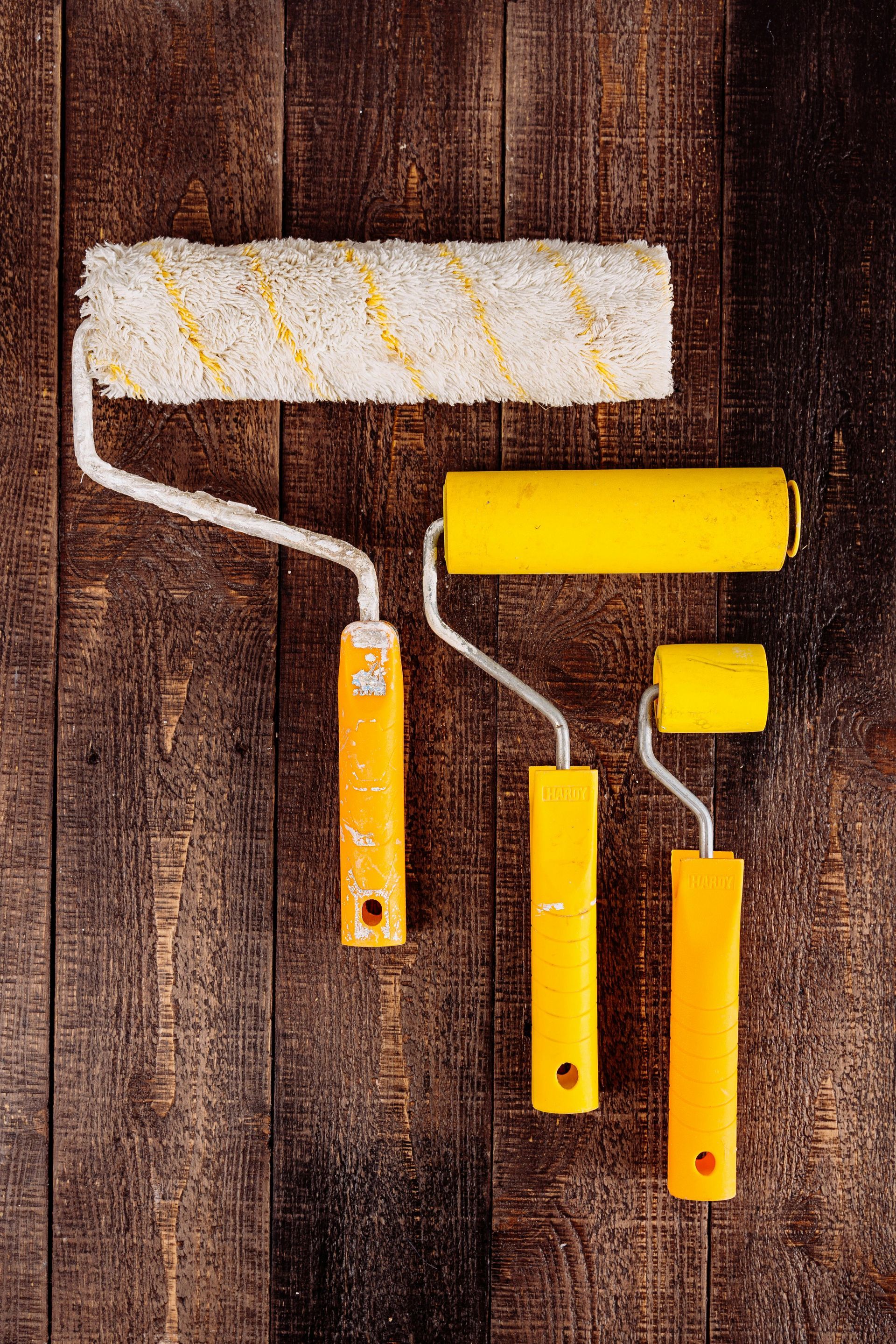 Three yellow paint rollers on a dark wood surface. The largest is at the top.