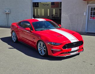 A red mustang with white stripes is parked in front of a garage.