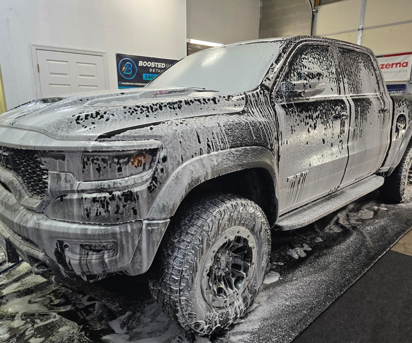 A dirty truck is covered in foam in a garage.
