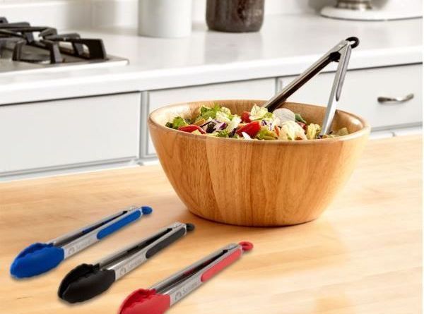 A wooden bowl filled with vegetables and tongs on a kitchen counter.