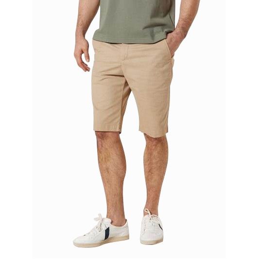 A man wearing khaki shorts and a green shirt is standing with his hands in his pockets.