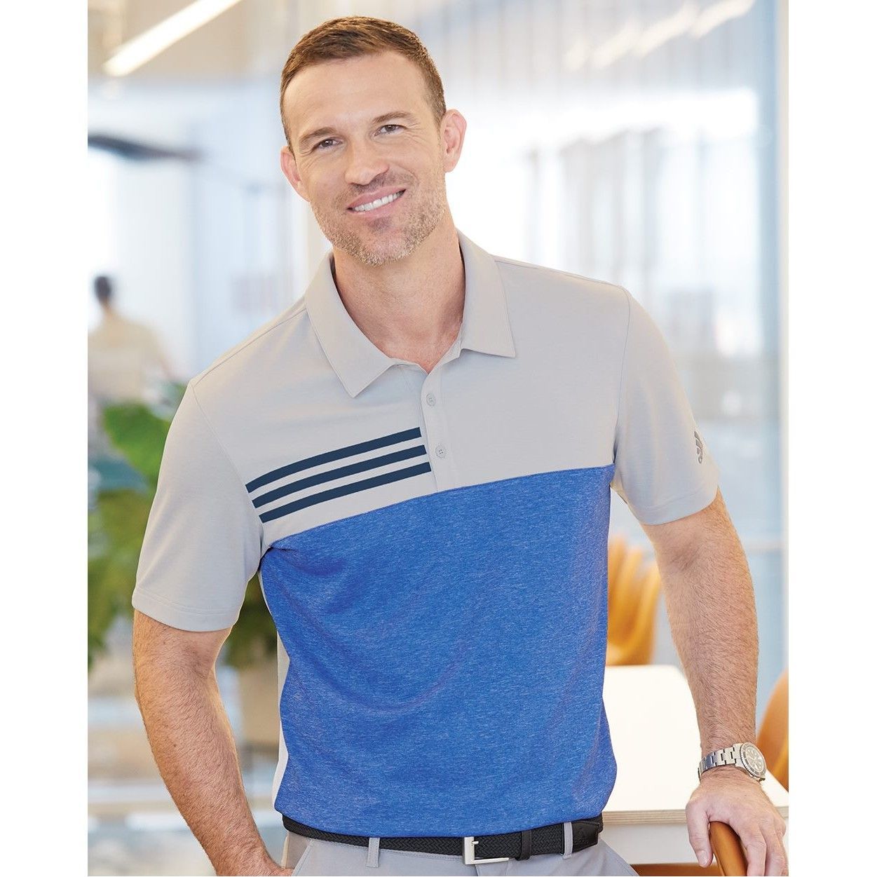 A man wearing a grey and blue polo shirt is standing in a room.