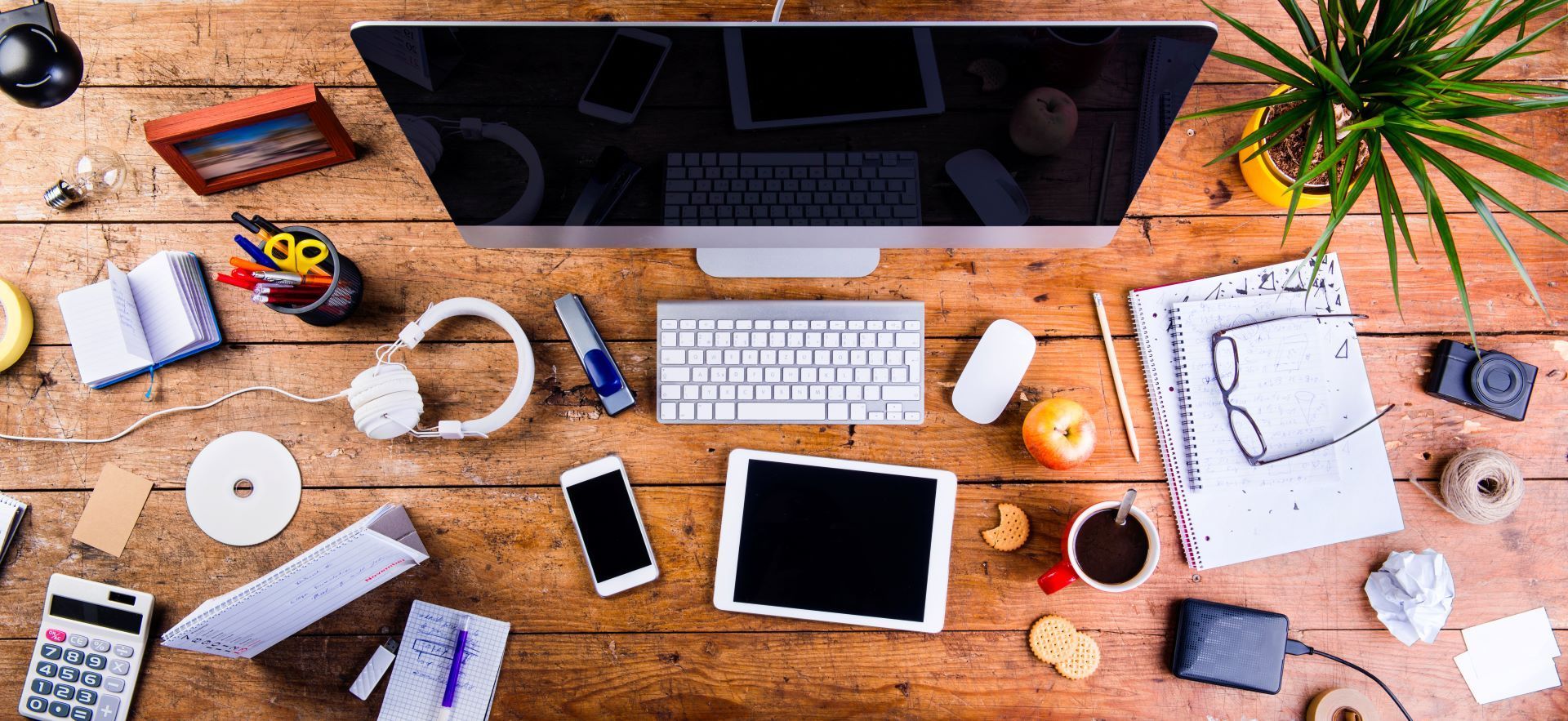 A wooden desk with a computer , keyboard , tablet , phone , and other electronics.