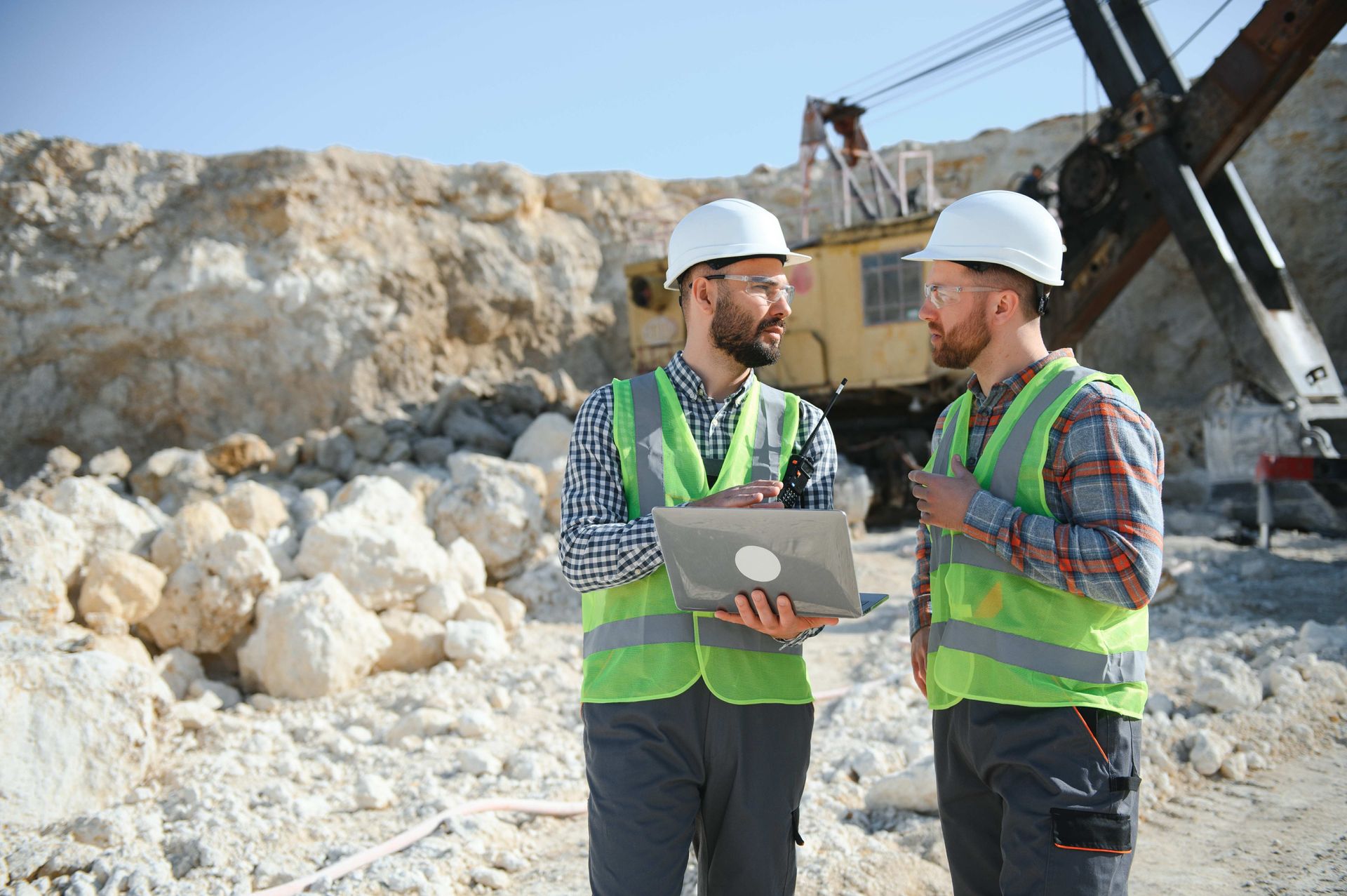 two construction workers are looking at a laptop in a quarry