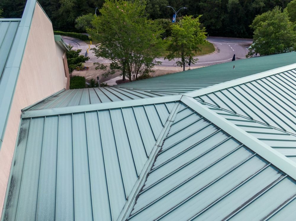 Overhead view of a house roof with dark gray asphalt shingles. A triangular dormer and chimney are visible.
