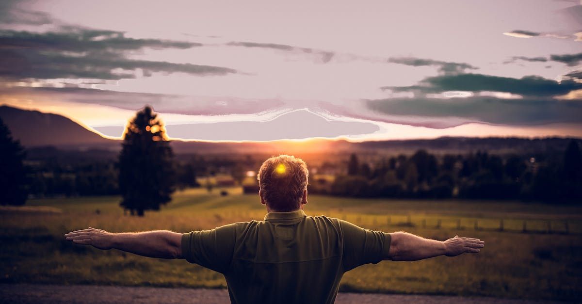 A man is standing in a field with his arms outstretched at sunset.
