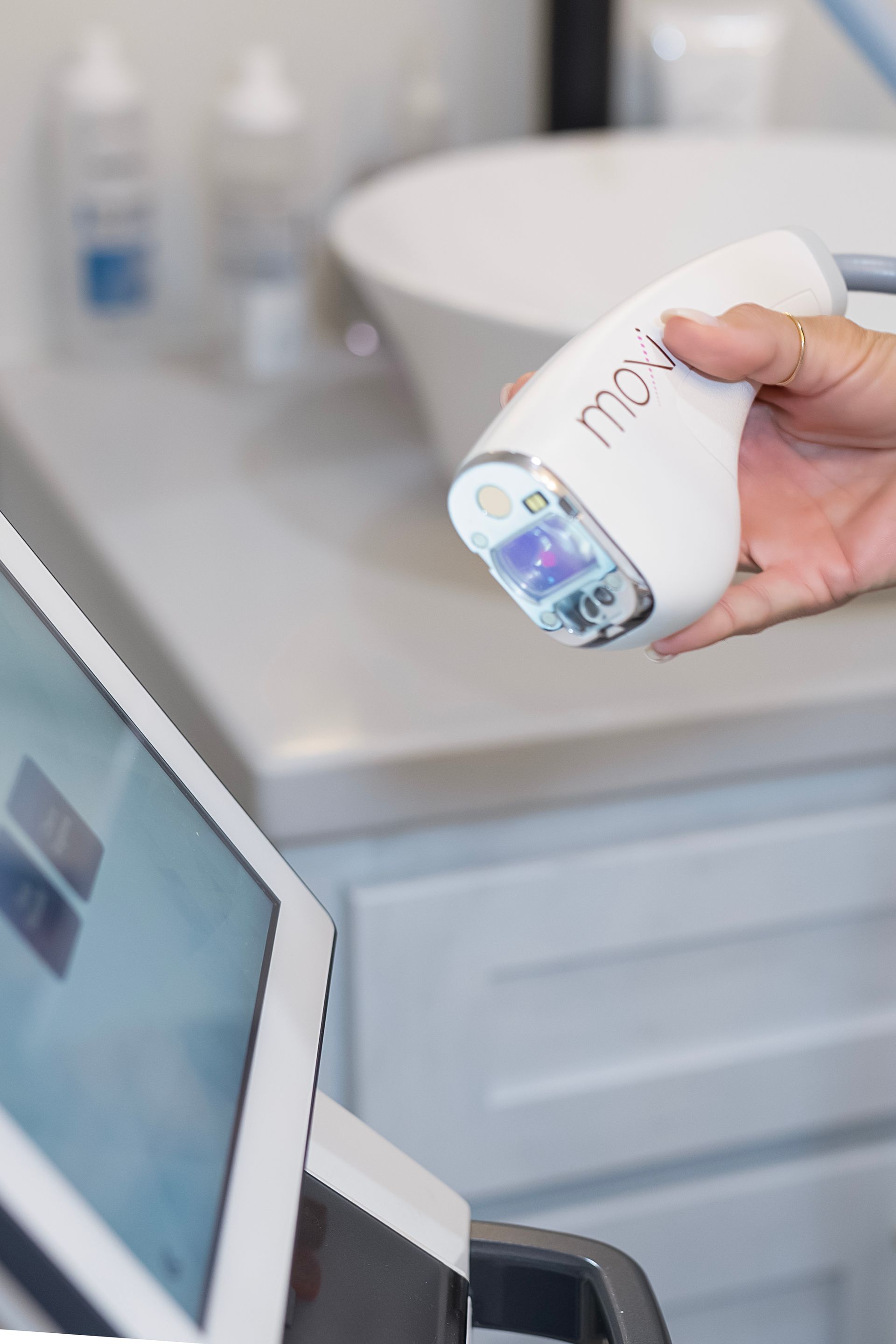 A person is holding a device in their hand in front of a monitor.