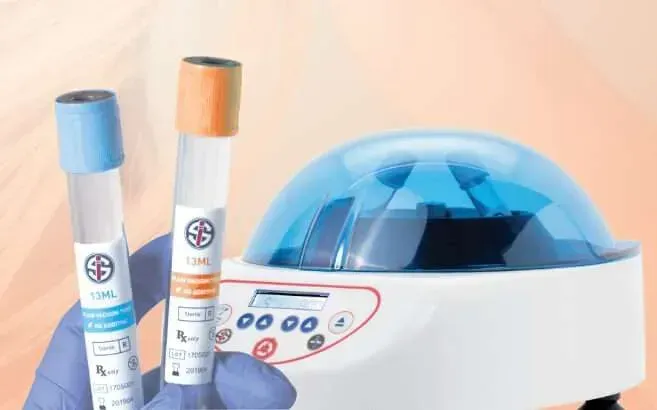 A person is holding two test tubes in front of a centrifuge.