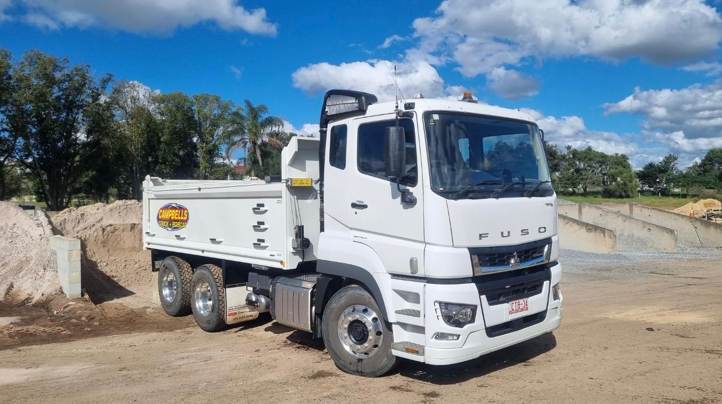 A White Dump Truck is Parked in a Dirt Lot — Campbell's Truck and Bobcat and Landscape Supplies In Gympie, QLD