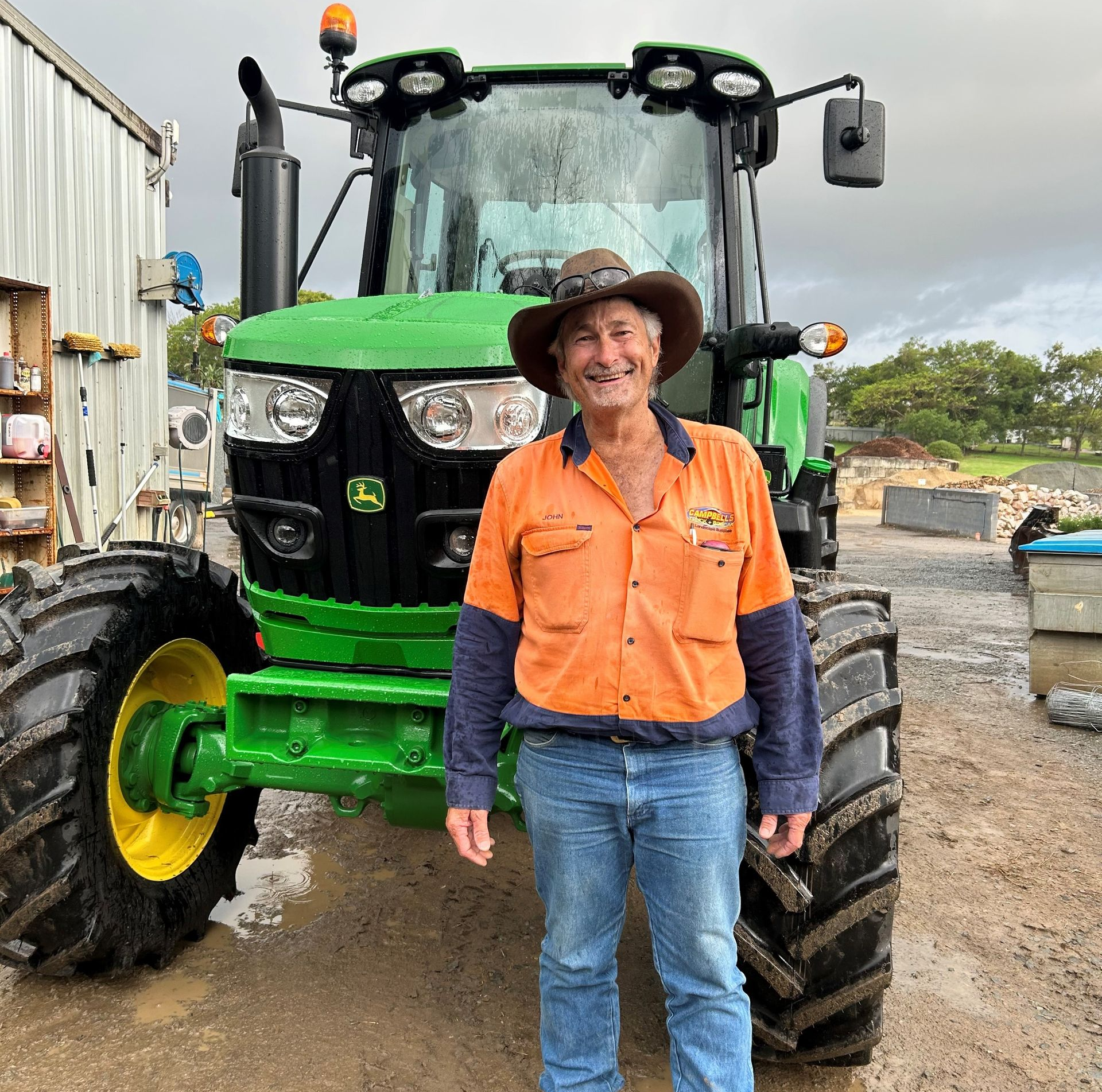 Man Smiles Beside a Green Tractor — Campbell's Truck and Bobcat and Landscape Supplies In Gympie, QLD
