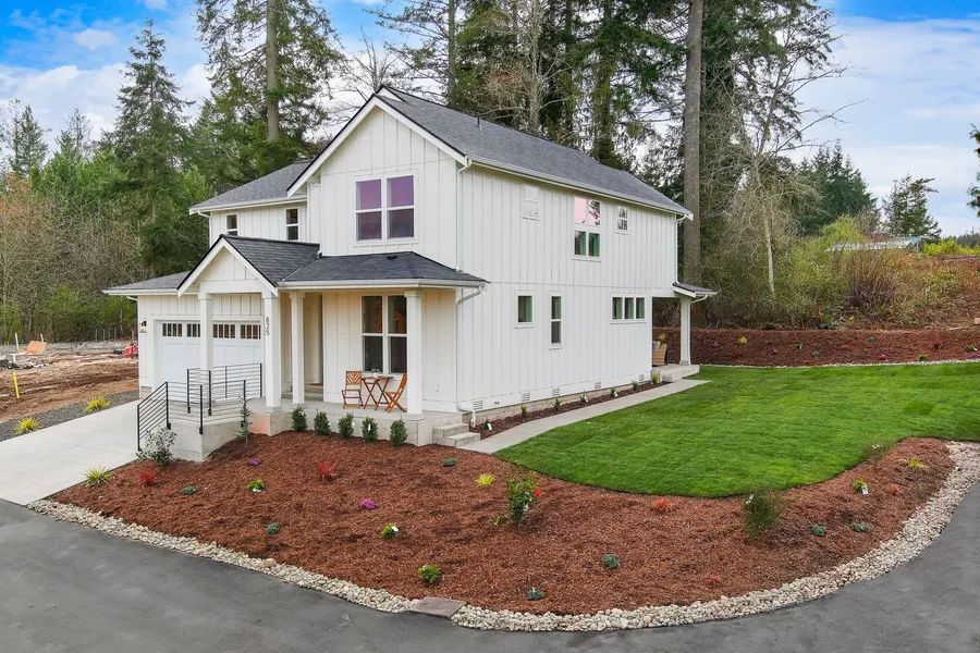 A white house with a black roof is sitting on top of a lush green hillside.