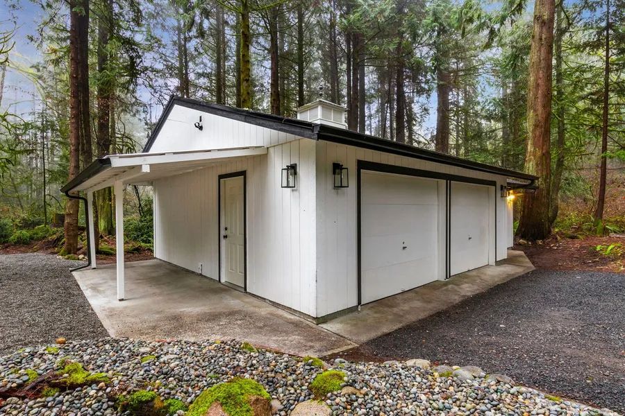 A white garage with a canopy in the middle of a forest.