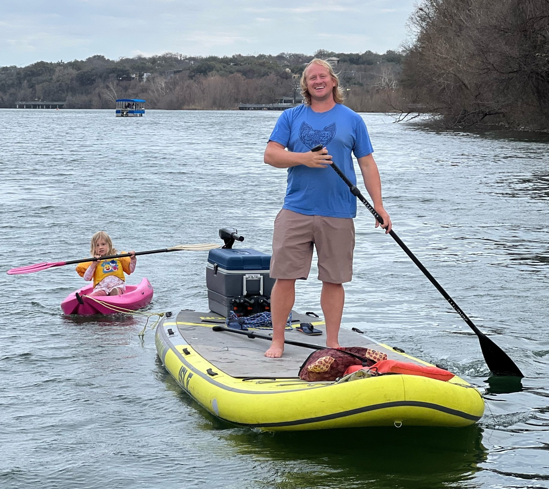 A man is standing on a paddle board next to a little girl in a kayak