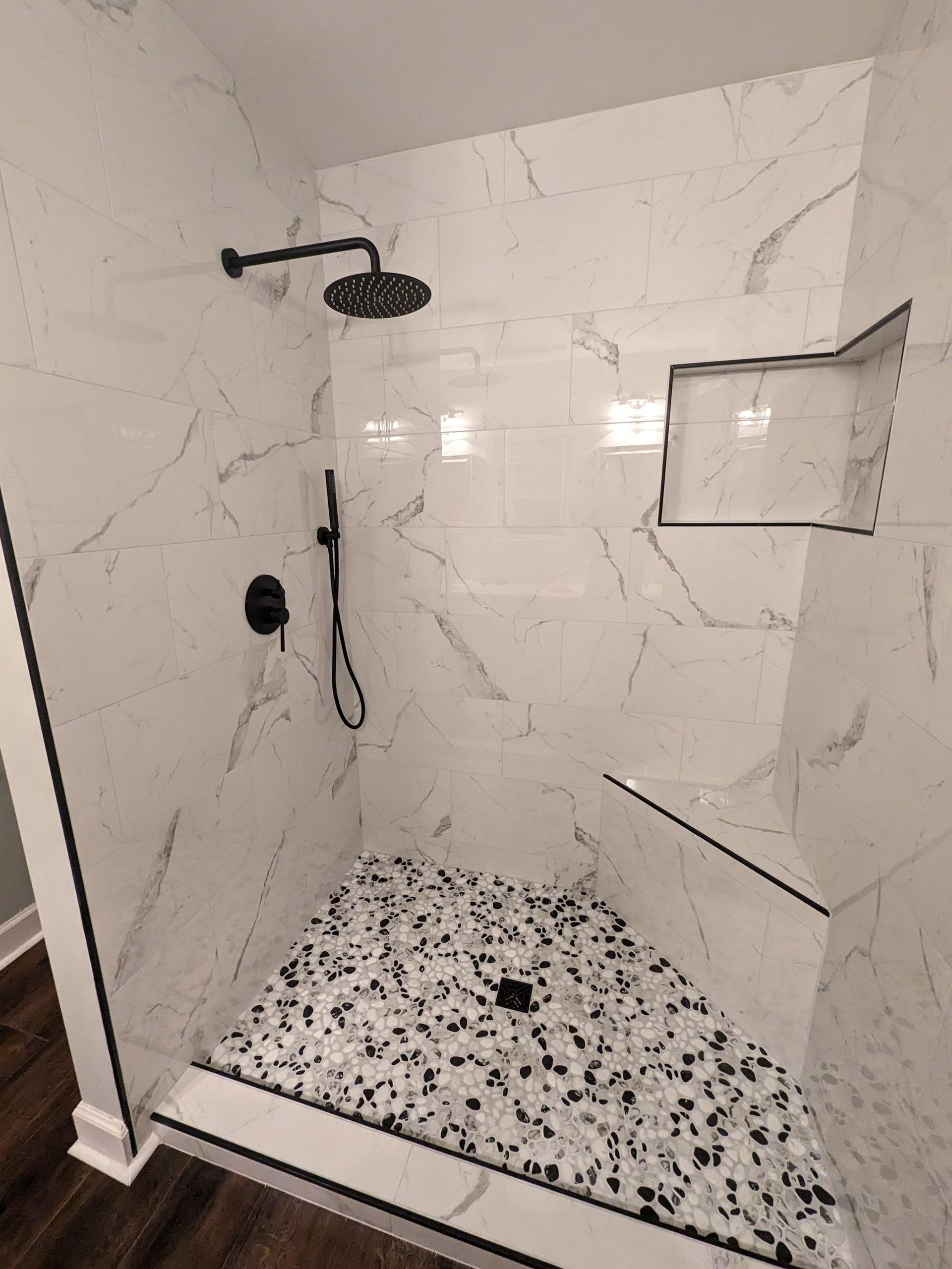 A walk in shower with a shower head and a tiled floor.
