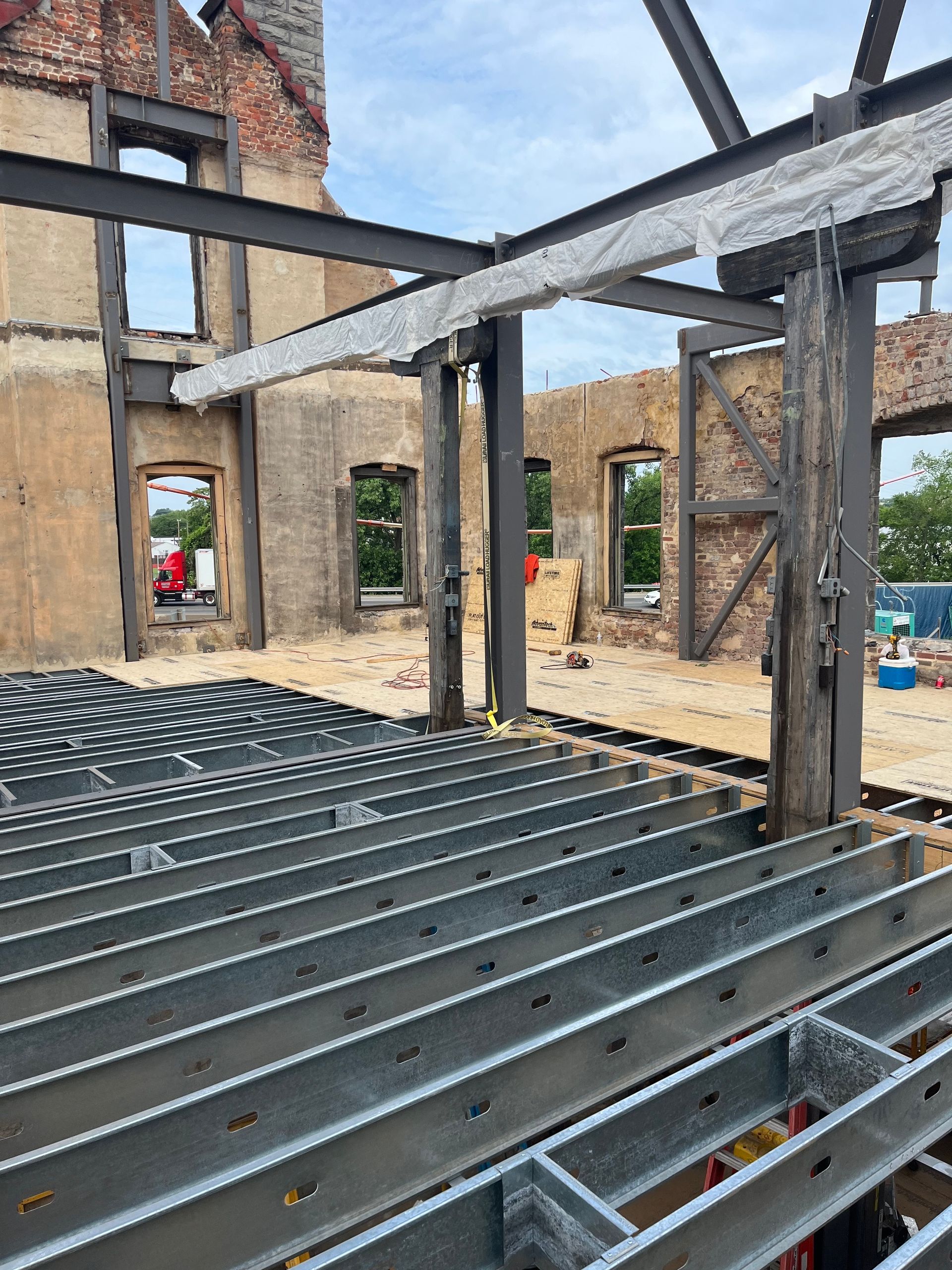Partially built building interior with exposed steel beams, brick walls, and floor joists.