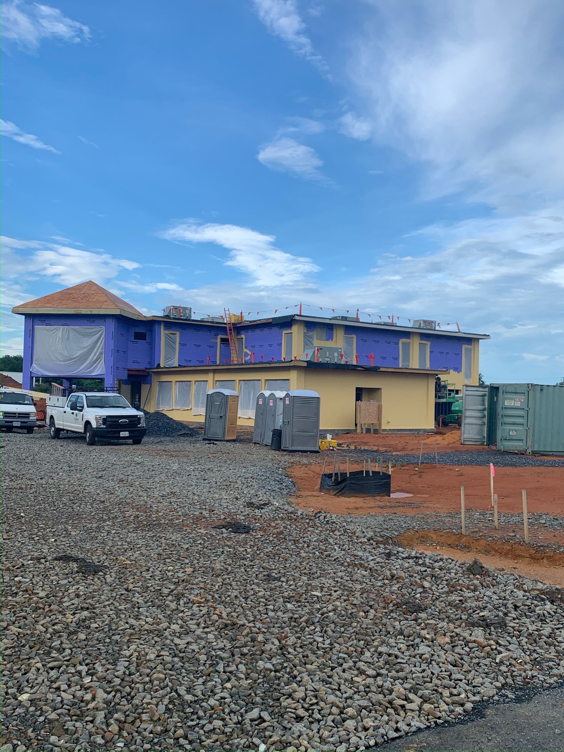 Partially built blue two-story house with gravel foreground and cloudy sky