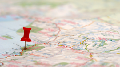 paper map with a red thumbnail stuck in it