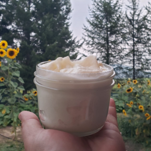 Hand holding a small jar of whipped cream outdoors, with sunflowers and trees in the background