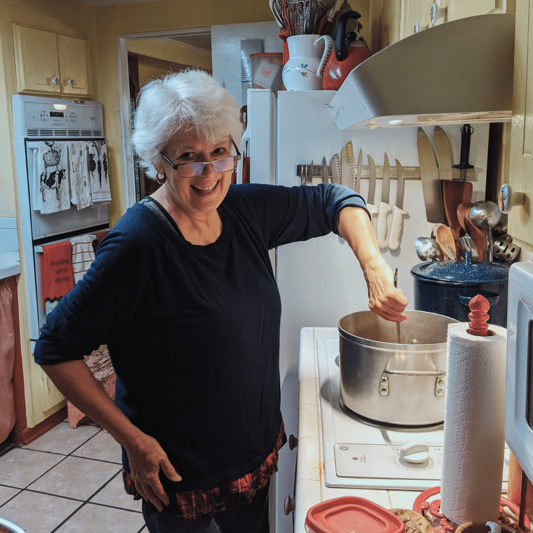 woman in a kitchen looking at the camera while stirring a large pot on the stove
