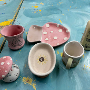 Assorted handmade ceramic cups and bowls on a blue surface, including pink and cream pieces with polka dots.