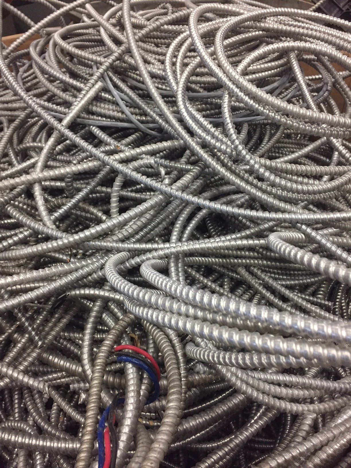 Heap of coiled silver metal hoses or flexible conduits with a few red and blue wires visible
