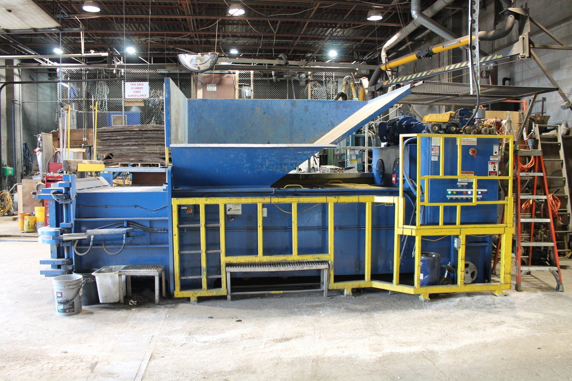 Blue industrial machine with yellow railings in a factory warehouse