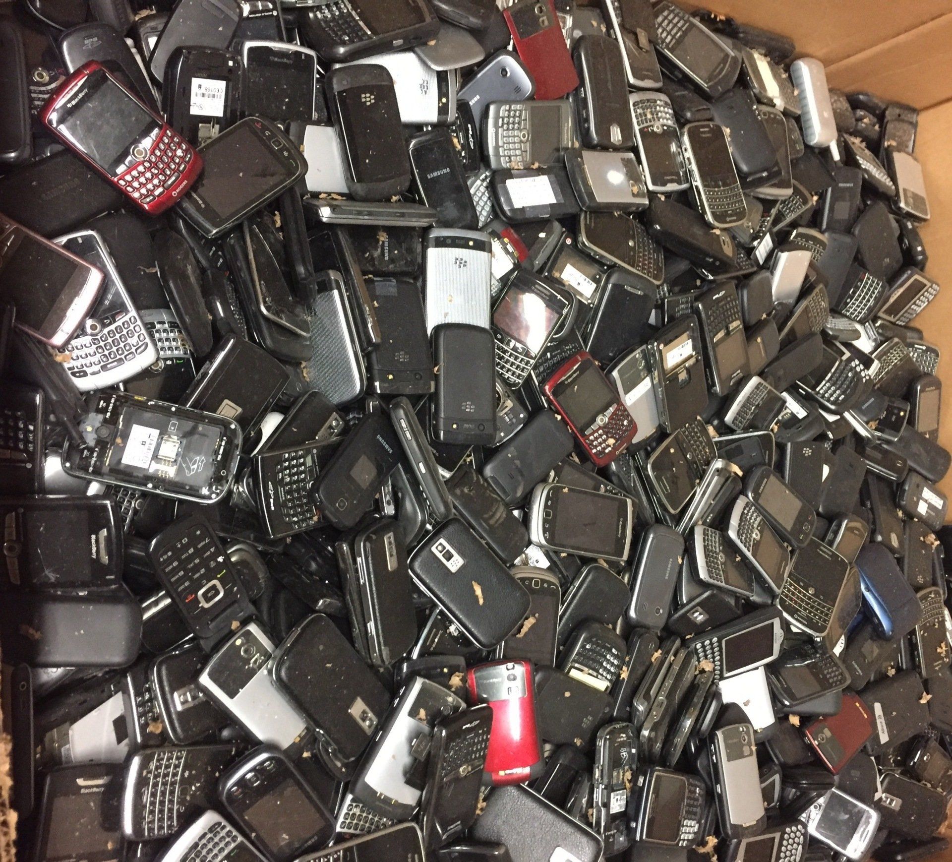 Pile of assorted old mobile phones and electronics, mostly black and silver with a few red devices.
