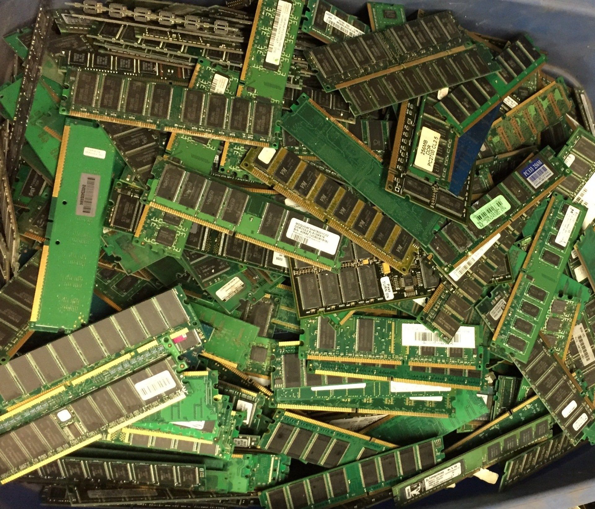 A pile of green and black computer RAM sticks scattered in a container.