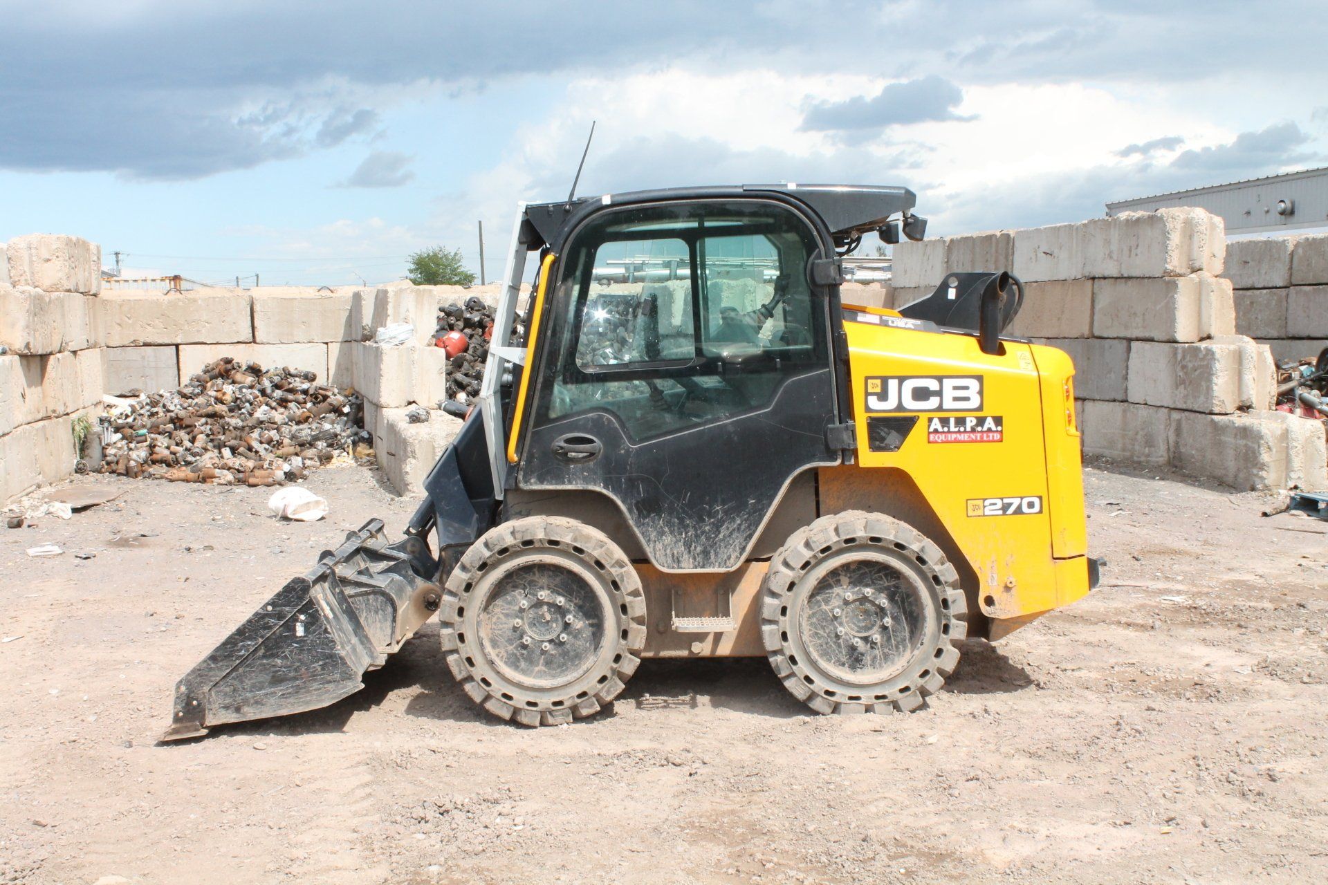 Yellow JCB skid-steer loader with front bucket in a dusty construction yard