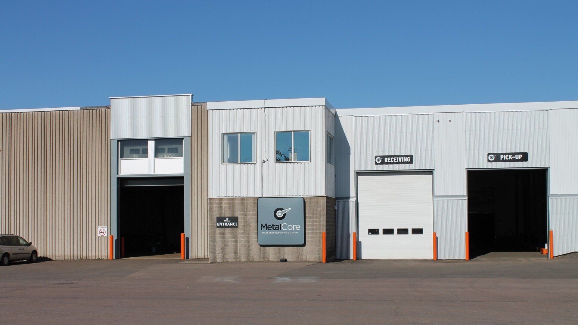 Industrial warehouse building with two open garage bays and a beige-and-white facade under a blue sky