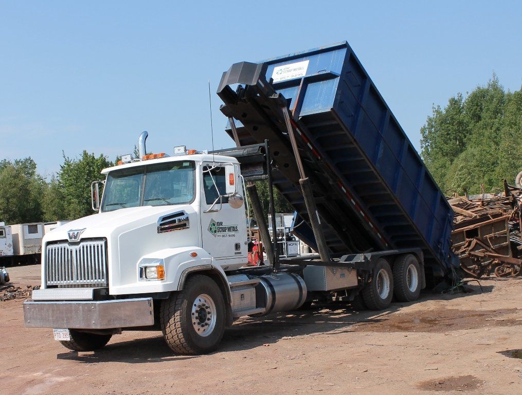 White dump truck with raised blue bed at a dirt worksite, loaded with scrap wood and debris.