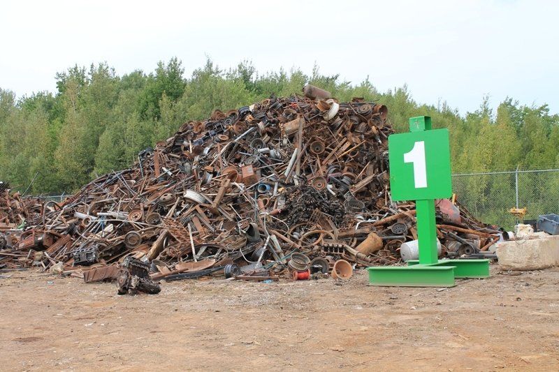 Large pile of scrap metal in a yard beside a green sign marked “1”