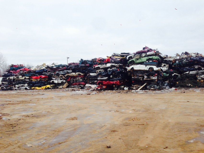 Stacks of crushed cars piled in an outdoor junkyard under a cloudy sky