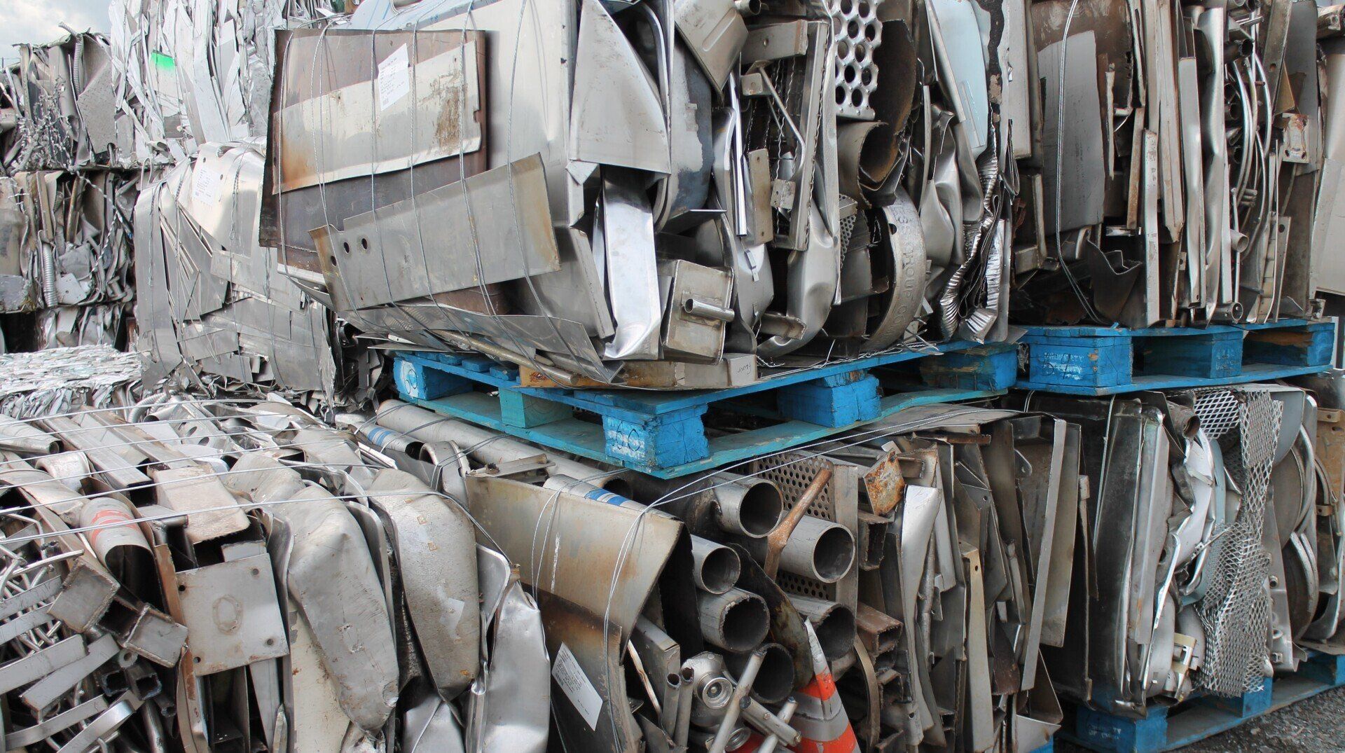Stacked scrap metal and pipes on blue pallets in a recycling yard