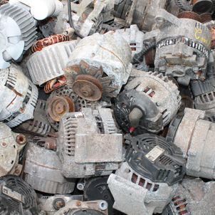 Pile of used electric motors and alternators, mostly gray and dusty, stacked in a scrap heap