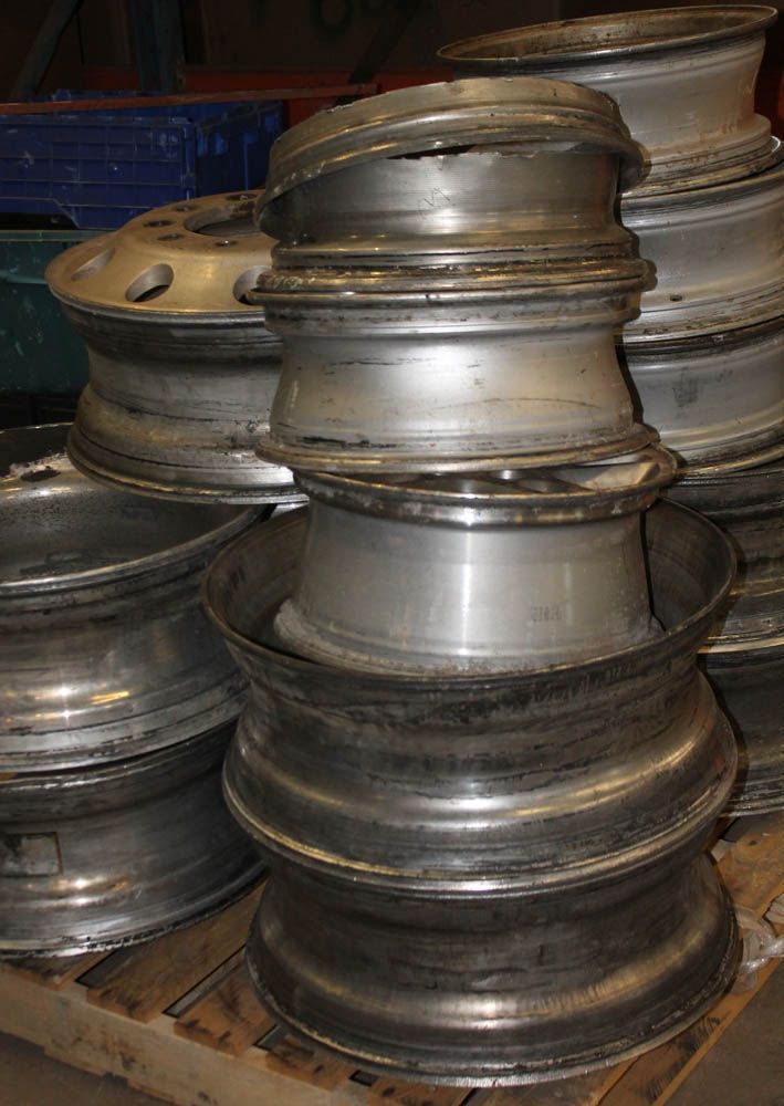 Stacks of used metal wheel rims and tires piled on a wooden pallet in a workshop or scrapyard.