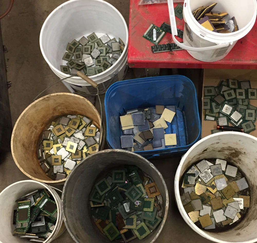 Buckets of assorted electronic chips and circuit parts arranged on a floor and red table.