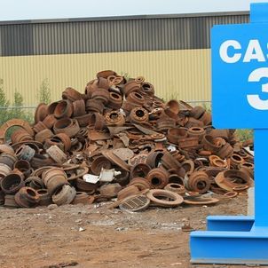 Pile of rusted metal parts beside a building, with a blue sign partially visible on the right.