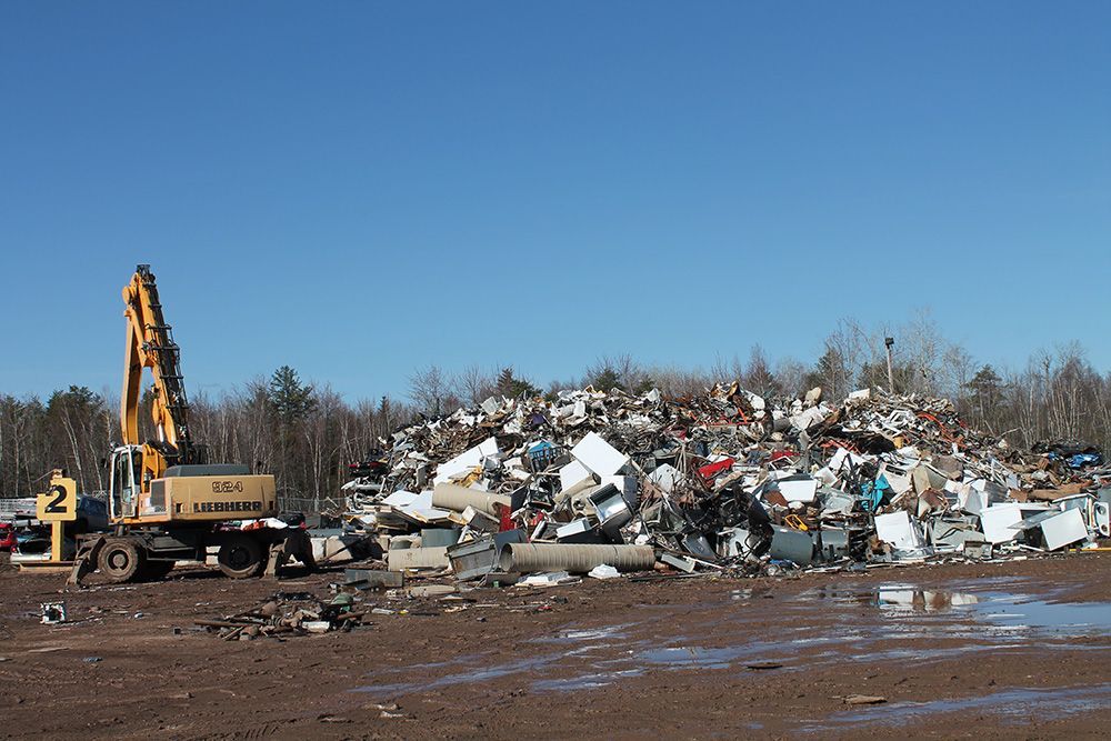 Bulldozer at a scrapyard, moving a large pile of crushed metal under a clear blue sky