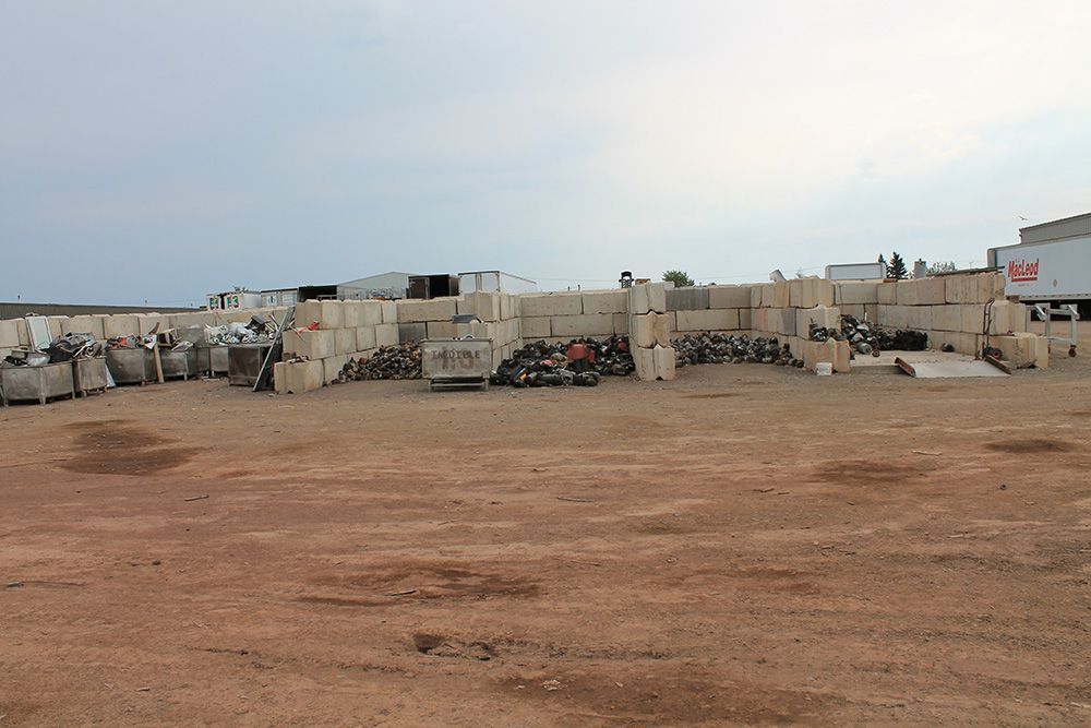 Wide dirt lot with stacked concrete blocks and a few construction vehicles under a cloudy sky